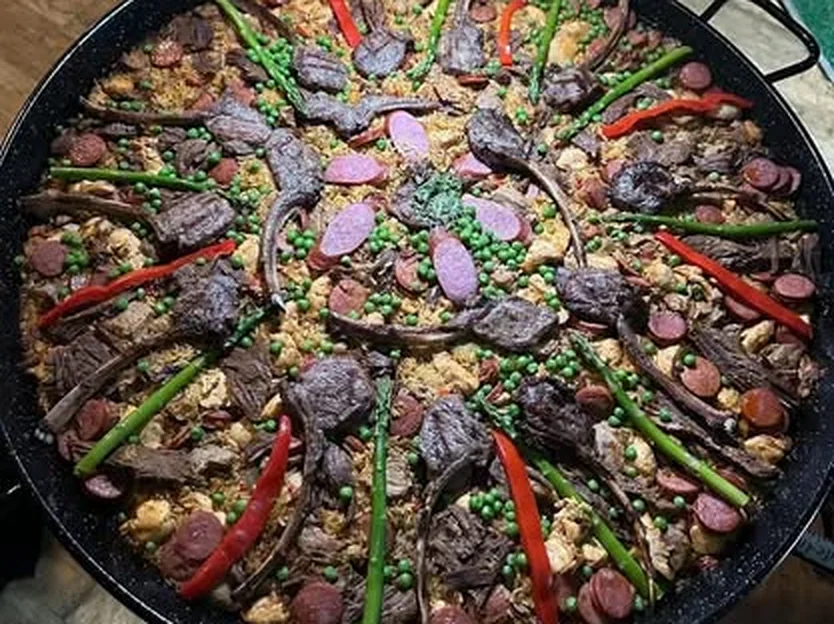 Paella con costillas de cordero, chorizo y espárragos servida en la paellera